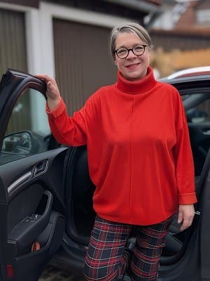 Frau Wenger im rotem Pullover steigt mit einem Lächeln aus Auto.